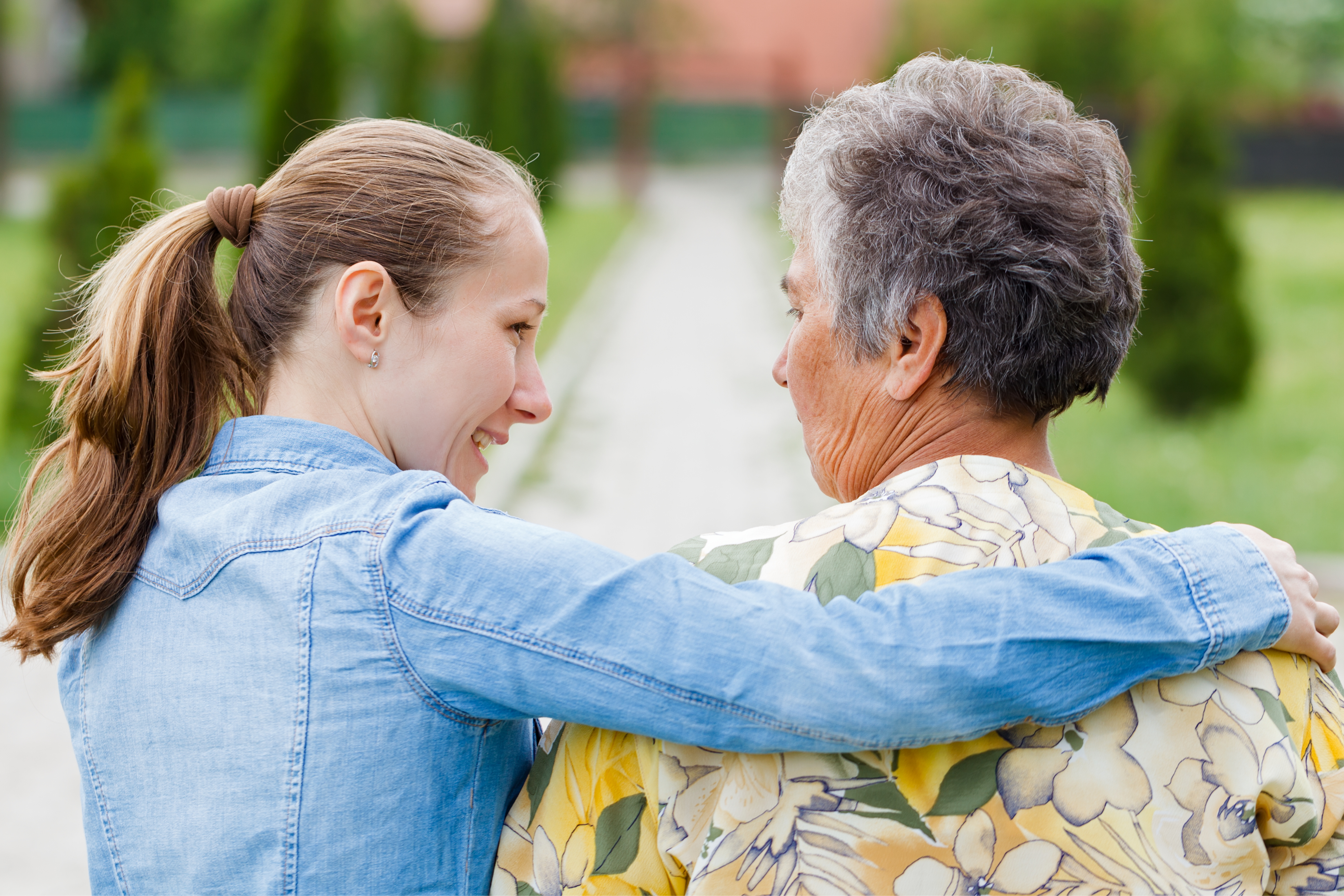 A young woman shares a light moment with an elderly woman outside in the garden, illustrating meaningful companionship and community bonding.