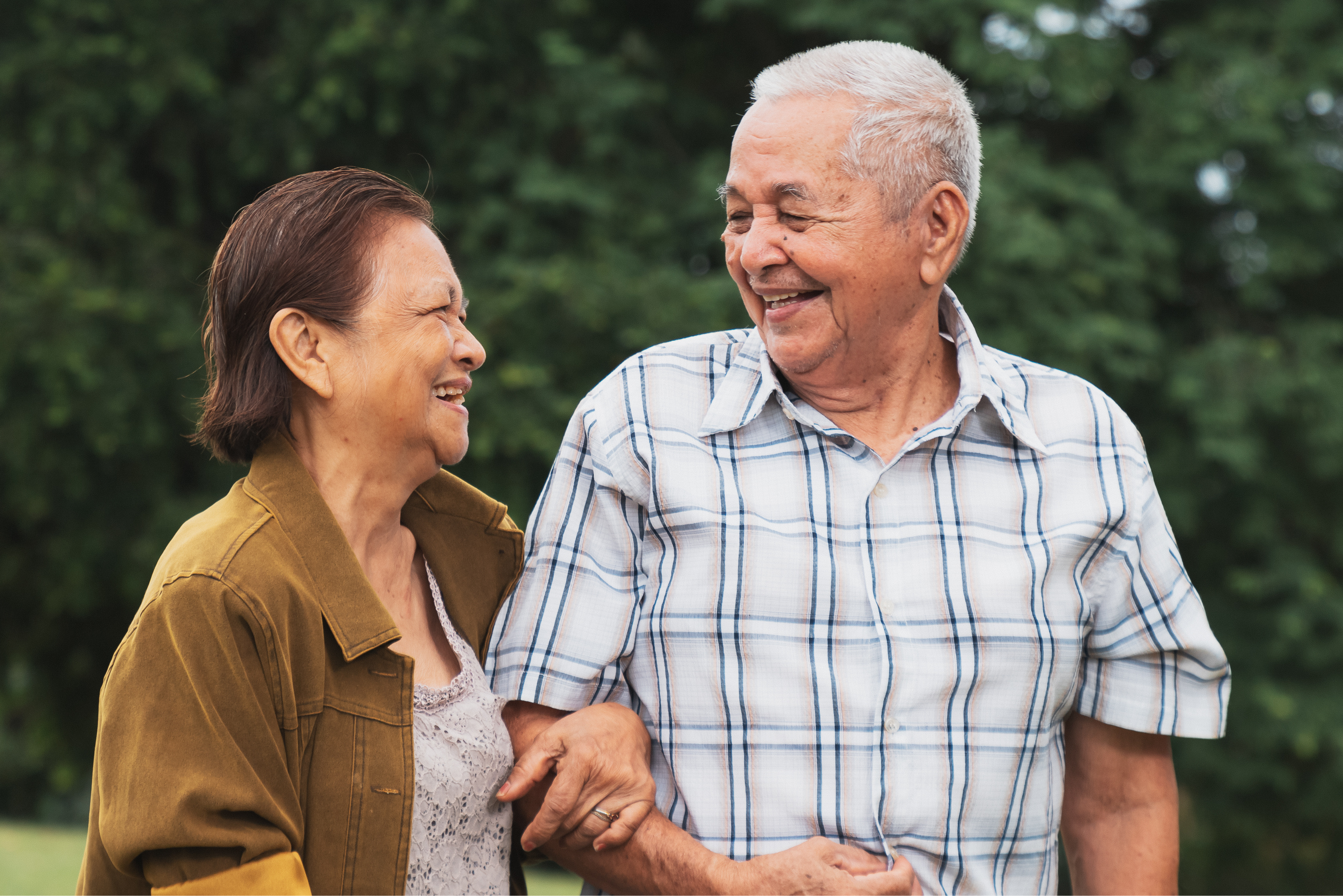A joyful older couple strolls together, smiling and relaxed, symbolizing independence, connection, and peace of mind in a supportive living environment.